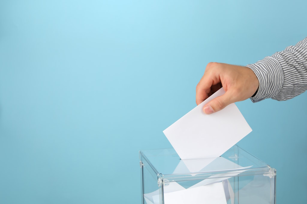urnas_votos_Por AtlasComposer_man-putting-ballot-into-voting-box-on-blue-backgro-2021-09-02-22-33-14-utc_envato